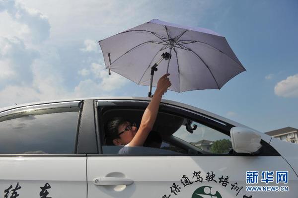 7月20日，在浙江省臨安市一家駕校內(nèi)，一名學(xué)員在車(chē)頂架著遮陽(yáng)傘的教練車(chē)內(nèi)練習(xí)。
