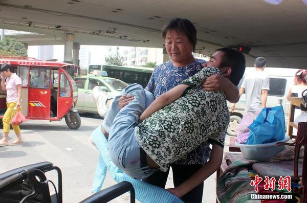 來到街頭“賣唱”點(diǎn)，呂愛梅熟練地把兒子把下三輪車，布置場(chǎng)地。 馬義恒 攝