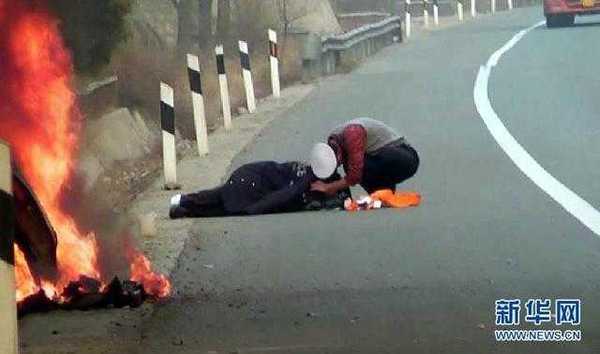 1月5日，青銀高速山西汾陽(yáng)段，一輛小轎車側(cè)翻在路旁的排水溝里發(fā)生自燃。車后20多米處，一名傷者躺在冰冷的地面上，渾身顫抖。接警趕來的交警查看傷情后，將自己的棉大衣脫下蓋在了傷者身上。圖為交警梁麗青(右)將自己的棉大衣脫下蓋在了傷者身上(視頻截圖)。