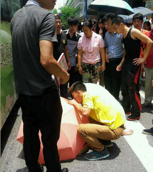 涉事公交車所屬公司相關(guān)負(fù)責(zé)人表示，事故原因警方正在調(diào)查中，該公司將會負(fù)責(zé)阿婆的醫(yī)藥費。圖為阿婆被抬出，有街坊給她撐起一把傘，等待救護車。目擊者供圖