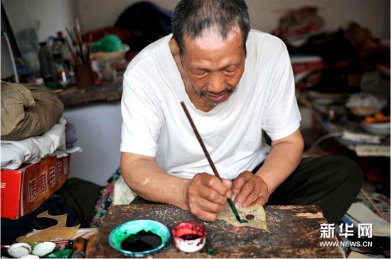 6月5日，張奎老人在為雕刻好的皮影上色