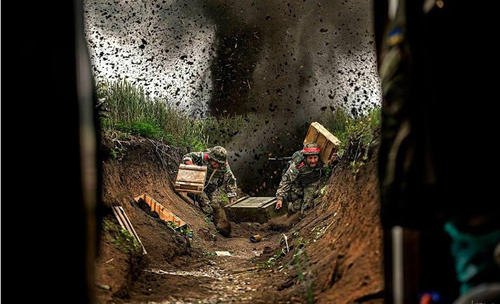 遭到炮擊的烏軍塹壕，兩名士兵正冒著炮火搬運彈藥箱。