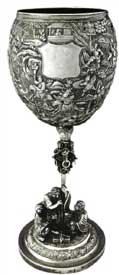 征戰(zhàn)圖高腳杯   Standing Trophy with Battle Scene Pattern 晚清 通高：29cm；口徑：9.5cm；底徑：10.6cm；重:681g 款識(shí)：慎昌，LW   清代中晚期，隨著外銷銀器的逐漸升溫，銀匠不僅開始借鑒青銅器、瓷器的特征創(chuàng)造銀器，更融合進(jìn)宗教思想及豐富的想象力。征戰(zhàn)圖高腳杯的杯身運(yùn)用錘揲工藝由內(nèi)向外敲擊出隋唐故事“羅通掃北”浮雕圖，在杯身中央位置留有一醒目光面盾牌，用以鏨刻購(gòu)買者家族族徽，一方面彰顯其身份地位，另一方面也能夠起到防盜的作用。整體造型極具藝術(shù)感，杯托被設(shè)計(jì)成一只展翅翱翔的雄鷹，杯桿被設(shè)計(jì)成配有圓環(huán)的錫杖造型。底座焊接一打坐羅漢和一伏虎抱杵羅漢，底座整體設(shè)計(jì)成須彌山的造型，須彌山在印度佛教中象征著世界之中心，整體做工精湛，布局巧妙，體現(xiàn)了銀匠的藝術(shù)造詣與佛教思想的融合。