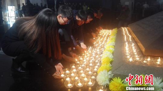 12月13日，沈陽“九一八”歷史博物館在國家公祭日舉行悼念儀式。圖為民眾向寓意民族英烈浩氣長存的金字塔型臥碑敬獻燭火。　朱明宇 攝