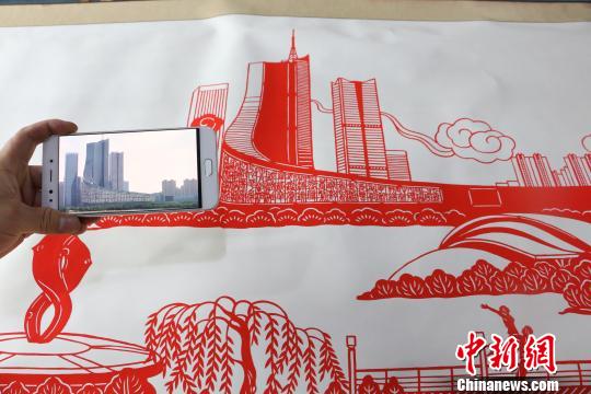 圖為丁健對(duì)比照片與剪紙作品?！∠默?攝